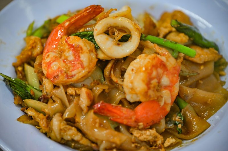 เส้นใหญ่ผัดกับกุ้ง หมึก และผัก ในจานสีฟ้า