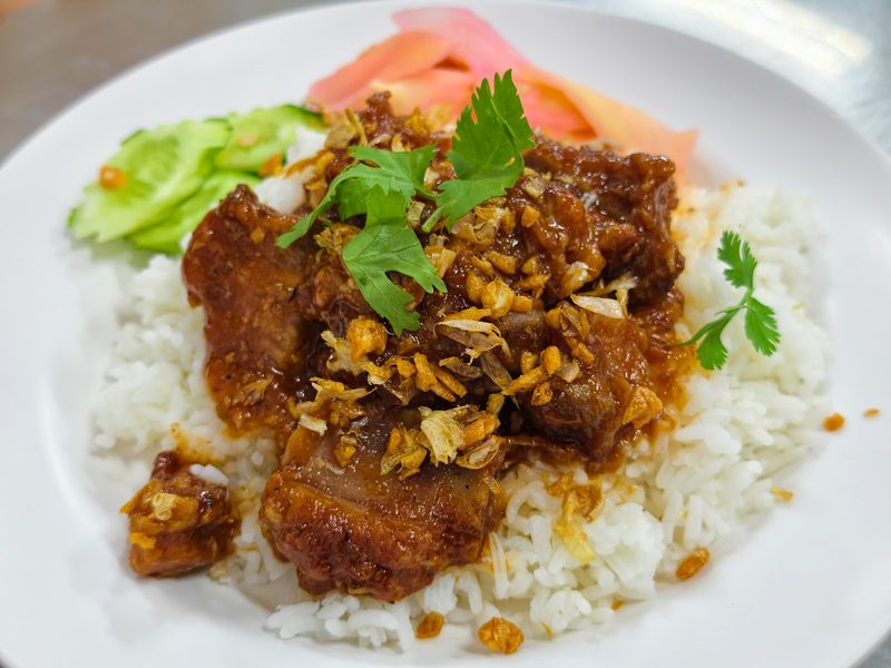 ซี่โครงหมูราดซอสบนข้าวสวย โรยกระเทียมเจียวและผักชี มีขิงดองข้างจาน