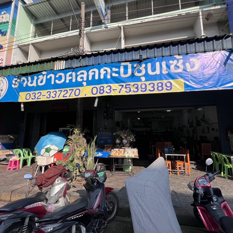 หน้าร้านตึกแถว ป้ายสีน้ำเงิน ร้านข้าวคลุกกะปิชุนเซ้ง พร้อมเบอร์โทร และรถจักรยานยนต์จอดหน้าร้าน