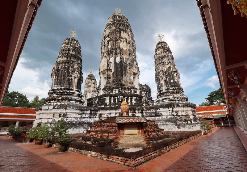ปรางค์สามองค์สีขาวเทาเรียงกันใต้ท้องฟ้ามีเมฆ มองผ่านกรอบประตู