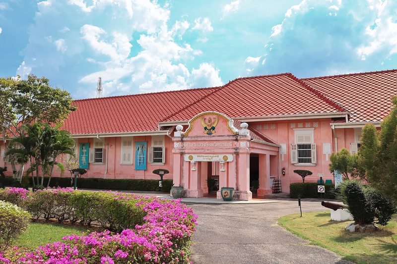 อาคารเก่าสีชมพูหลังคากระเบื้องแดง มีสวนดอกเฟื่องฟ้าด้านหน้า